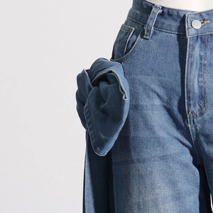 Détail d'un jean bleu à taille haute avec un grand nœud en denim et un bouton en métal