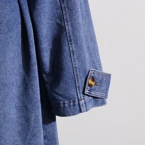 Detail of denim jacket cuff with contrast orange stitching and amber texture button