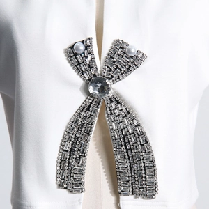 Detail of rhinestone bow brooch with pearls on white split sleeve t-shirt top