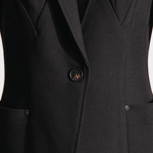 Detail of single tortoiseshell button and sleek metallic rivets on black blazer jacket