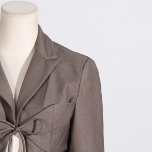 Detail of a brown cotton-linen blazer featuring a stylish tie-up bow and lapel collar