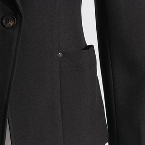 Detailed close-up of a black blazer featuring tortoiseshell button and metal stud accents