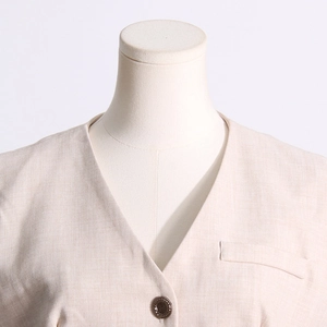 Vue détaillée du gilet crème à col en V montrant le tissu en lin et le bouton orné