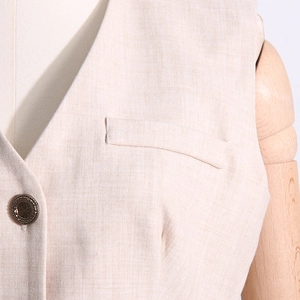 Détail du gilet beige clair avec col en V et fermeture par bouton en métal texturé vintage
