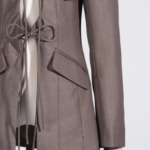 Detailed close-up of dark grey blazer with waist tie design and structured flap pockets