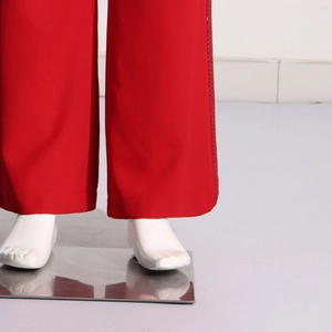 Detail of red wide-leg trousers showing rhinestone trim on the hem and side seam