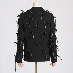 Detailed back view of a black blazer featuring multiple satin bow accents and buttoned cuffs