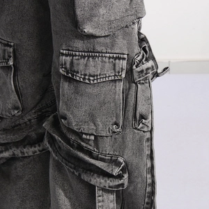 Detailed close-up of multi-pocket cargo jeans featuring washed grey denim and strap design