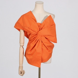 Detail of a bright orange blouse featuring a large sculptural bow and asymmetric neckline