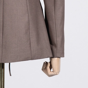 Detail of tan blazer fabric texture and precision tailoring on a wooden mannequin
