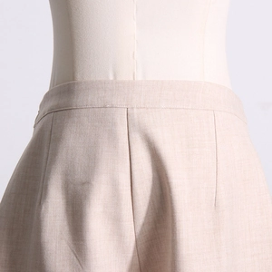 Détail de taille haute sur un pantalon beige avec plis nets et texture de tissu précise