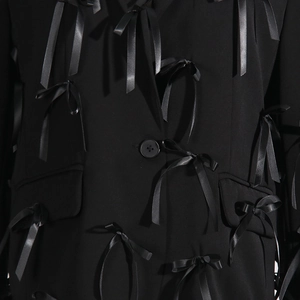 Close-up of 3D satin bow patchwork and button details on a black V-neck blazer