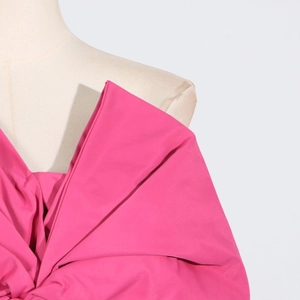 Detail of fuchsia asymmetrical top featuring oversized decorative bow and pleated texture