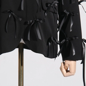 Detail of black V-neck blazer featuring elegant 3D satin bows and textured fabric finish