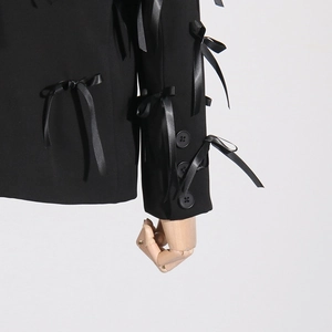 Detail of black blazer featuring 3D satin bows on sleeve and polished button cuffs