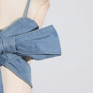 Detail eines hellblauen Denim-Tube-Tops mit großer Schleife und gelben Kontrastnähten