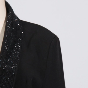 Dettaglio di paillettes nere e perline sul risvolto di una giacca con scollo a V