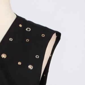 Detail of black sleeveless top featuring intricate gold and silver metal eyelet studs