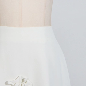 Detail of high-waisted white A-line skirt with 3D floral appliques and smooth texture