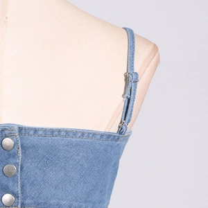 Detail von hellblauem Denim-Top mit verstellbaren Trägern und silbernen Metallknöpfen