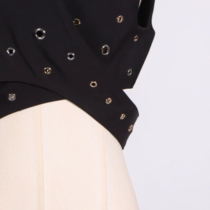 Macro detail of black sleeveless top featuring silver metal eyelets and crossover design