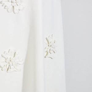 Detailed macro view of 3D floral appliqués on a high-waisted white A-line long skirt