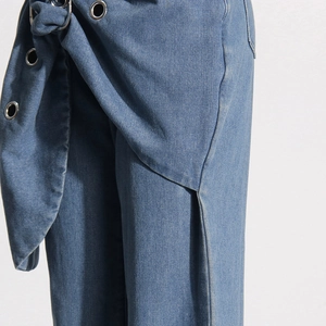 Detail of light blue denim jeans showing asymmetric waist wrap with metal eyelets and tie-up