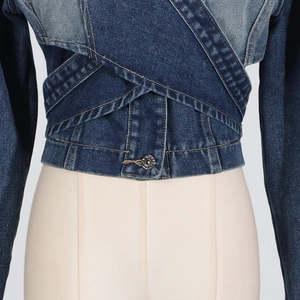 Macro detail of patchwork denim jacket featuring cross-waist design and metallic button