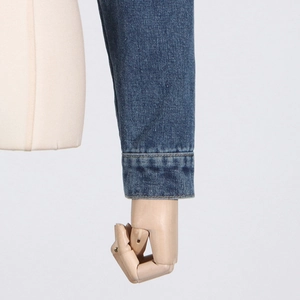 Detailed close-up of dark blue denim jacket cuff with neat stitching and twill texture