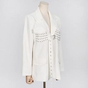 Detail eines weißen Oversize-Blazers mit silbernen Metallnieten und Ösengürtel für Damen