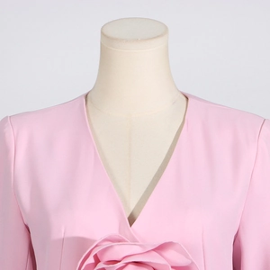 Detail of a light pink V-neck top featuring a large 3D fabric flower and smooth texture