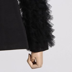 Close-up of layered tulle ruffles and pleated mesh cuffs on a black blazer sleeve