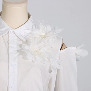 Detail der weißen Bluse mit 3D-Blumen, Federn und Perlenverzierung an der Schulter