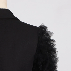 Detail of elegant black blazer featuring ruffled mesh patchwork and pleated shoulder texture