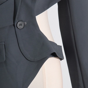 Detail of single-breasted dark gray blazer showing curved hollow-out waist and button texture