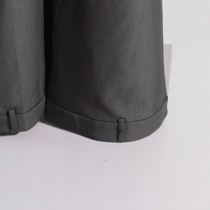 Vue détaillée du pantalon gris foncé montrant l'ourlet à revers, la patte boutonnée et le sergé