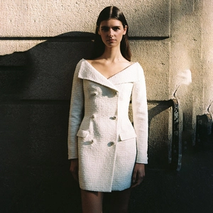 Close-up of cream white tweed fabric texture and decorative metal buttons on a short dress