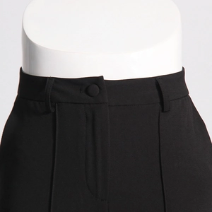 Detailed view of high-waist trousers featuring a fabric-covered button and belt loops