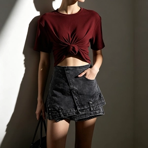 Détail du crop top bordeaux noué et de la jupe en jean grise asymétrique avec boucle