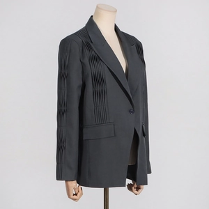 Detail of dark grey pleated blazer featuring unique structural accordion folds and lapels