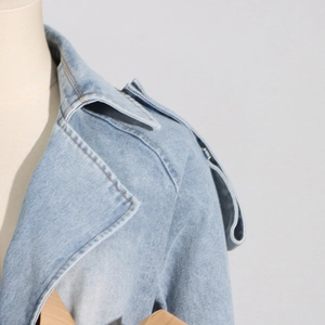 Detailed close-up of light blue denim jacket lapel and decorative shoulder strap detail