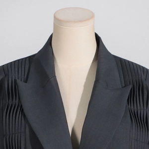 Detailed view of dark grey blazer featuring vertical pleated design and peaked lapels