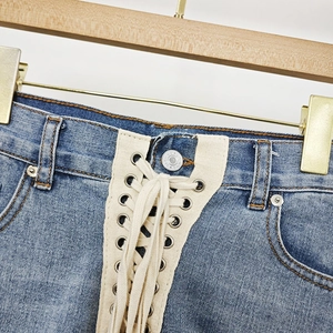 Detailed view of high-waist denim shorts featuring criss-cross lace-up design and silver eyelets