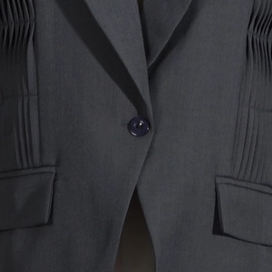Close-up of pleated detail and resin button on dark gray blazer with flap pockets
