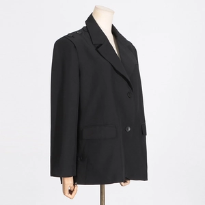 Détail d'un blazer noir mi-long avec boutons décoratifs aux épaules et poches à rabat