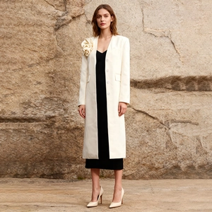 Detailed close-up of white long trench coat with 3D floral appliqué and lapel collar