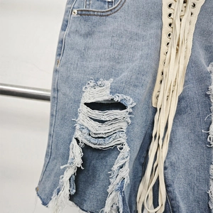 Detail of light blue denim shorts featuring large distressed rips and side lace-up ties