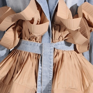 Detailed close-up of denim patchwork jacket with khaki pleated trim and waist tie strap