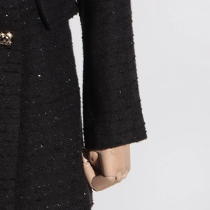Macro detail of black tweed fabric with shimmering sequins and embossed metal button