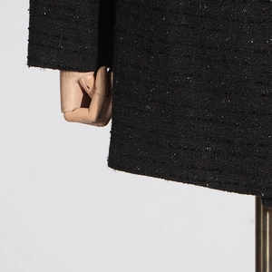 Close-up of black tweed fabric texture with shimmering metallic threads and woven details